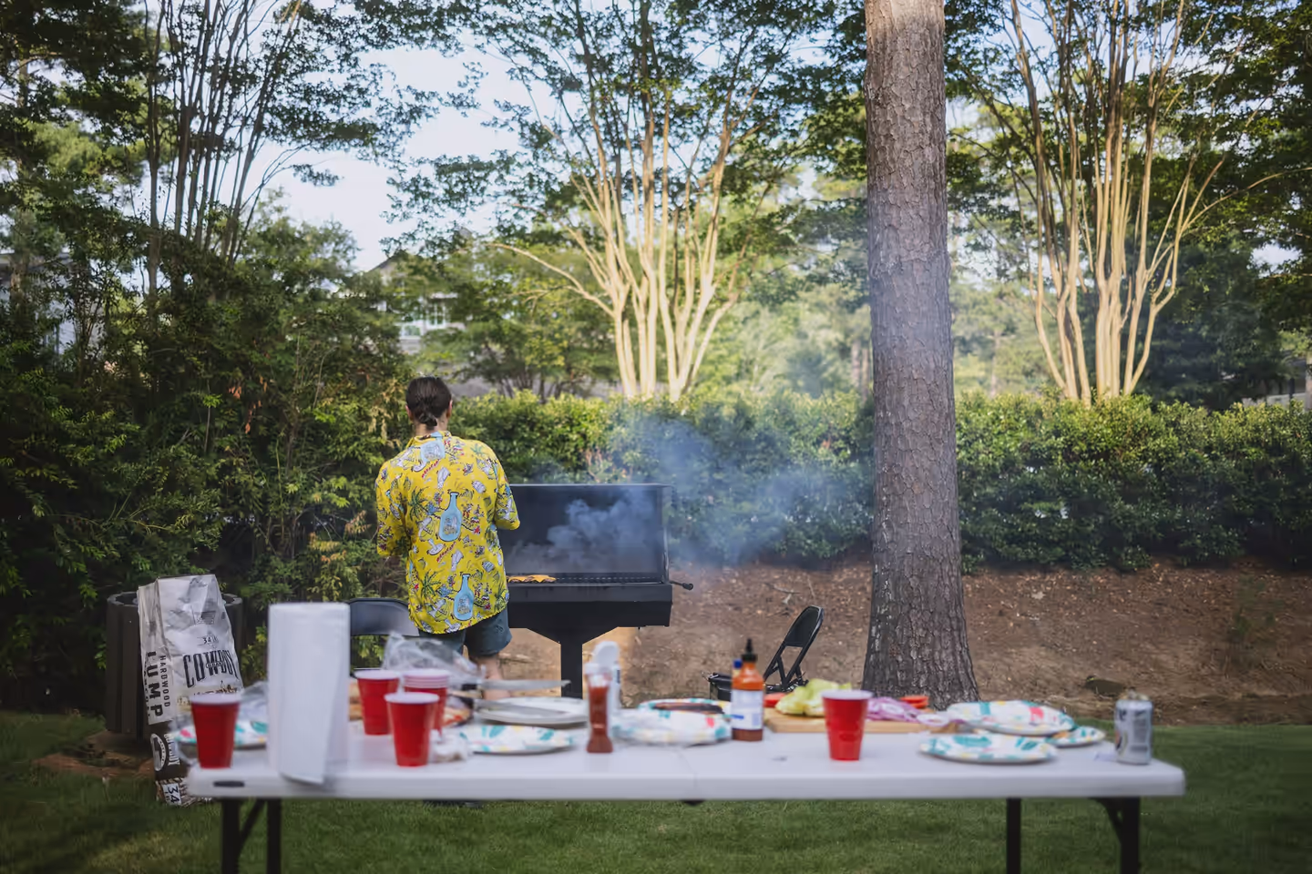 Pessoa na churrasqueira ao ar livre, com uma mesa de comida e bebidas em primeiro plano