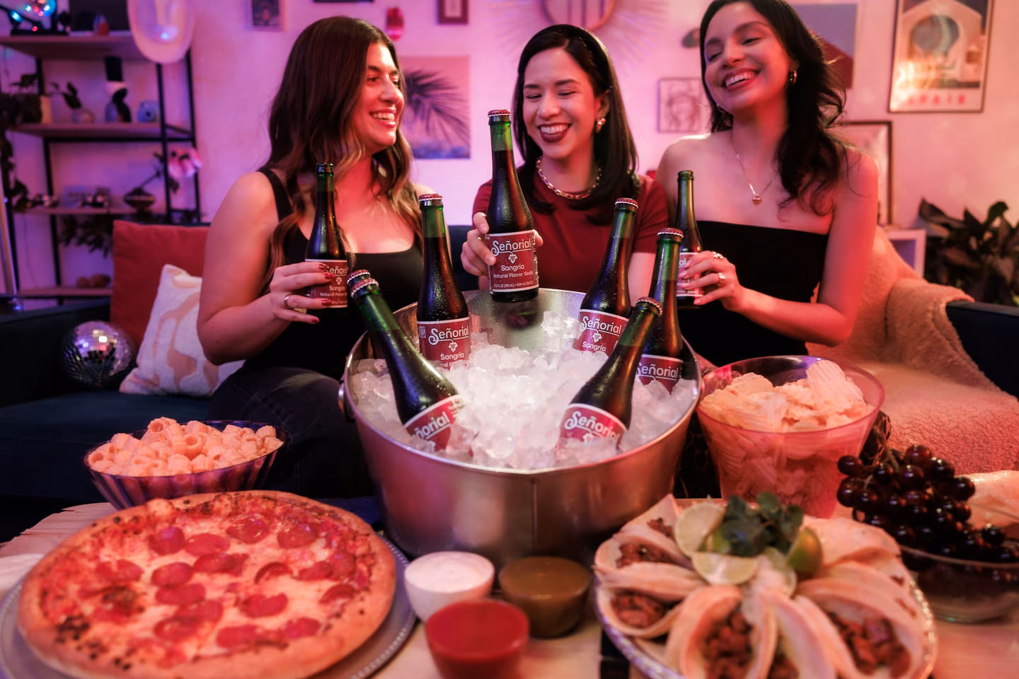 Três amigos rindo com cerveja e petiscos numa festa