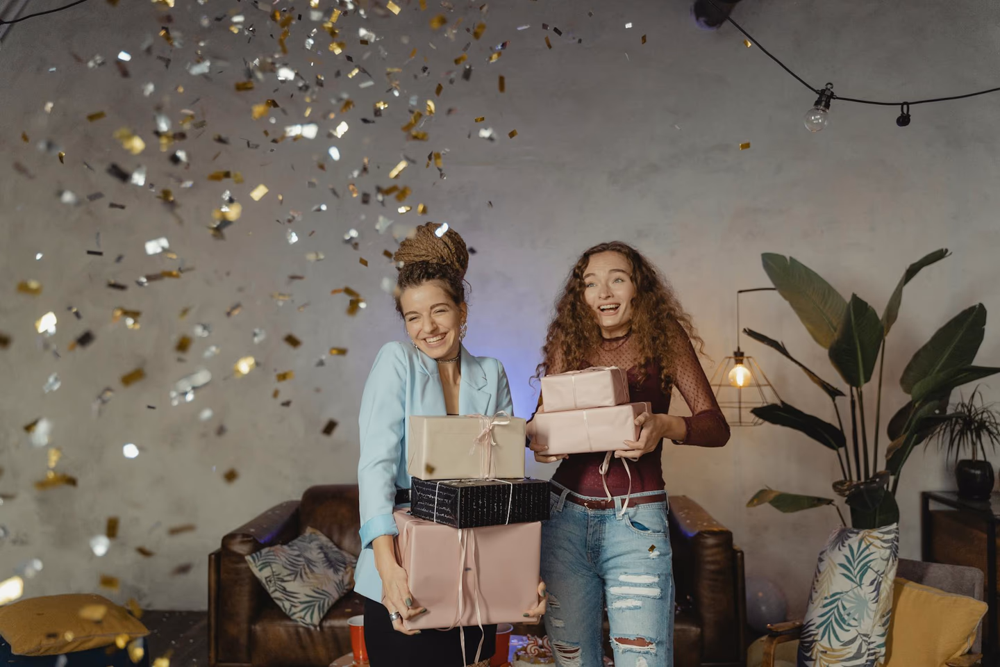 Two happy young women holding a stack of wrapped presents at a confetti-filled party